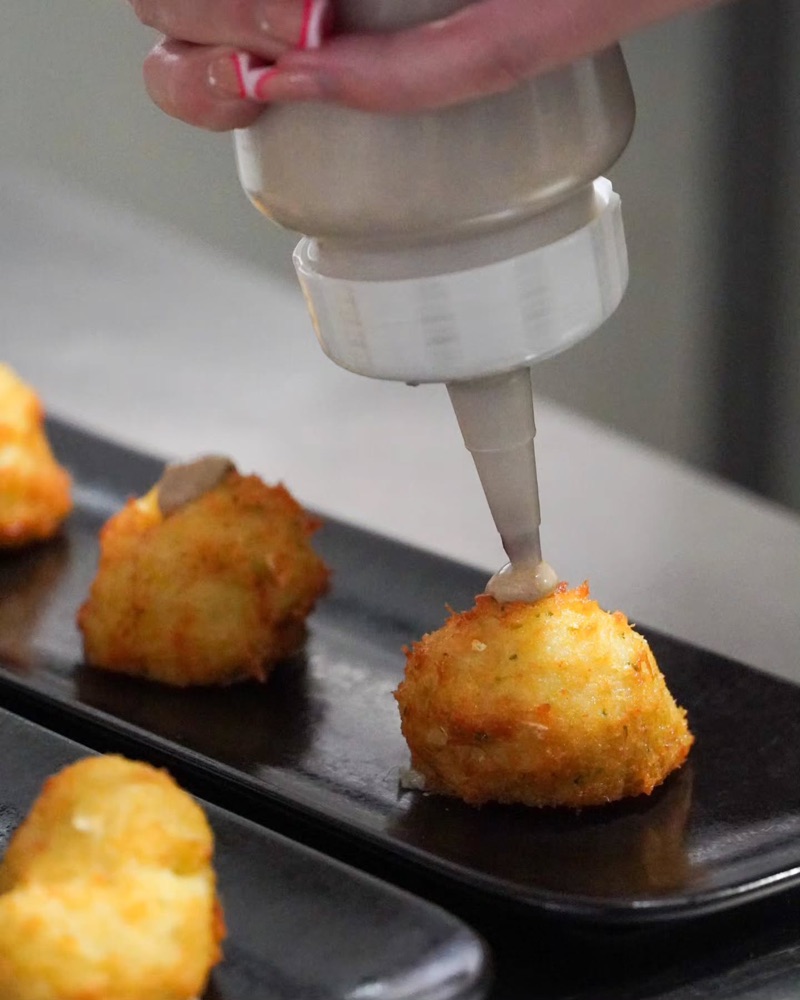 Algú posa salsa sobre unes croquetes amb un biberó de cuina