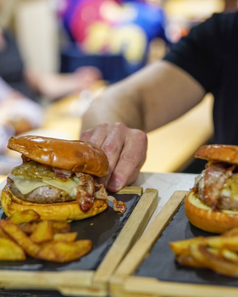 Una mà serveix una hamburguesa amb patates sobre una fusta