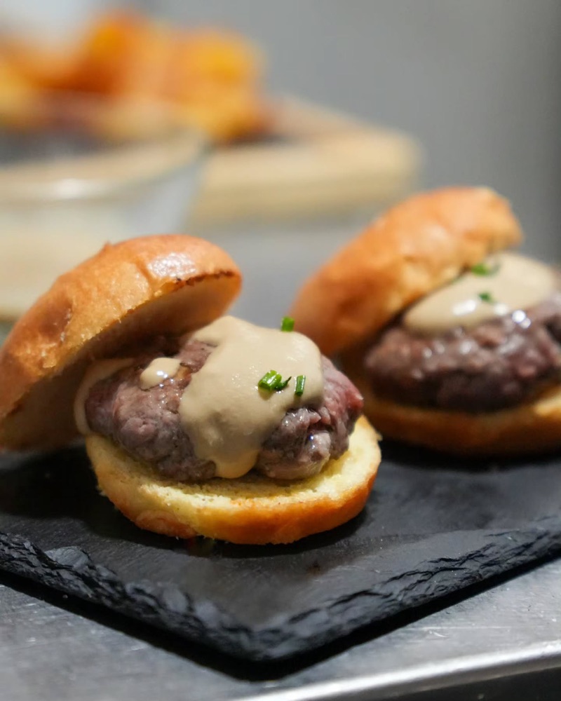 Dues hamburgueses petites amb salsa de formatge, sobre una pissarra