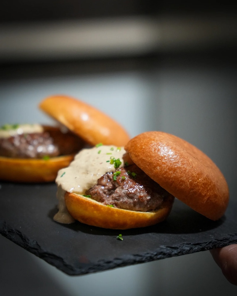 Una mà sosté dues hamburgueses petites sobre una pissarra