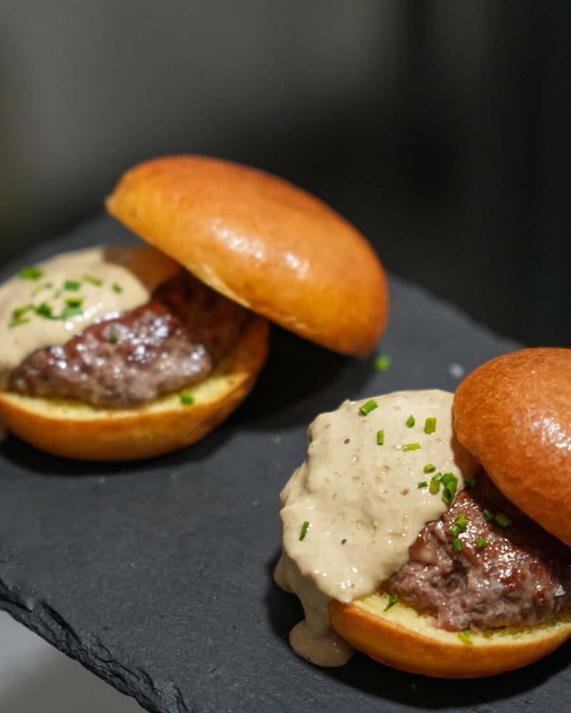 Dues hamburgueses petites amb salsa cremosa, sobre una pissarra