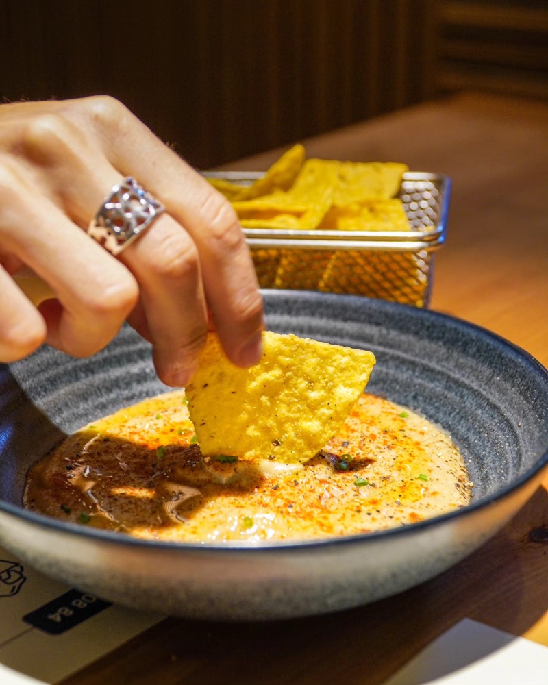 Una mà suca un nacho en un bol de crema
