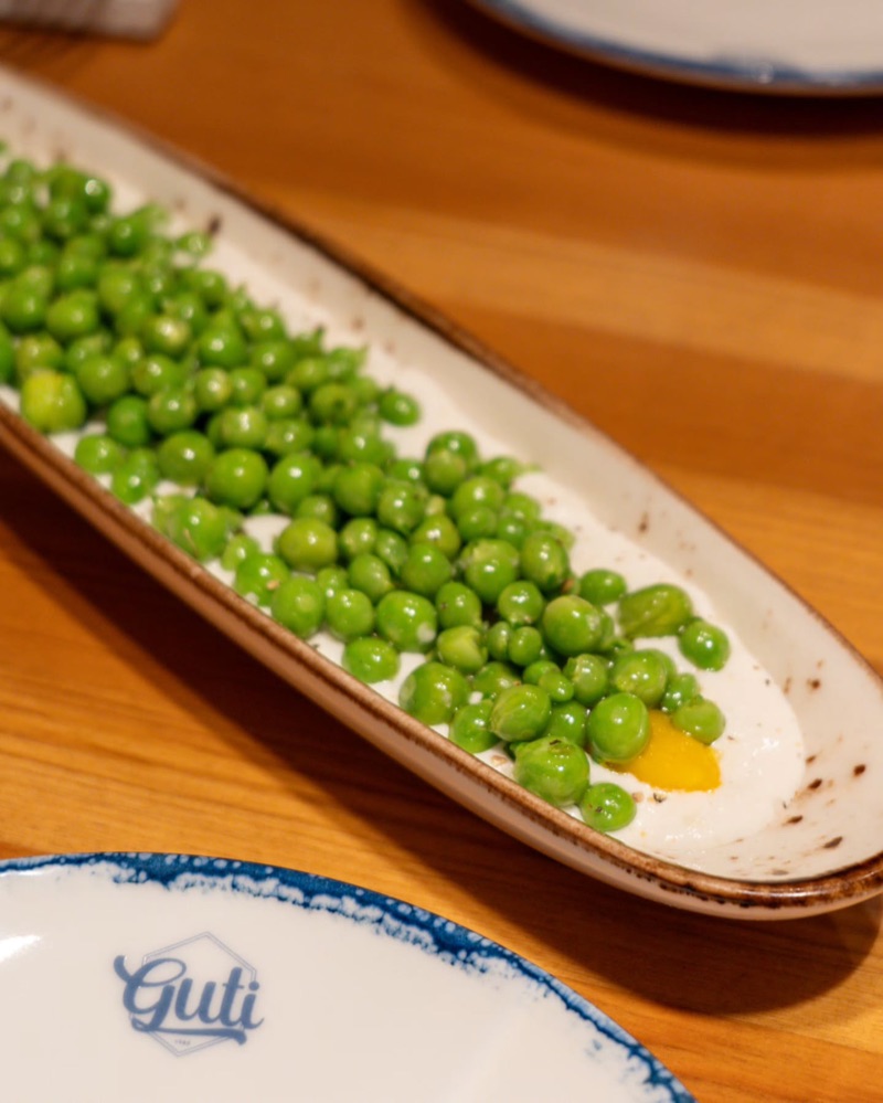 Pèsols amb rovell d’ou en una plata allargada, al costat d’un plat del Guti