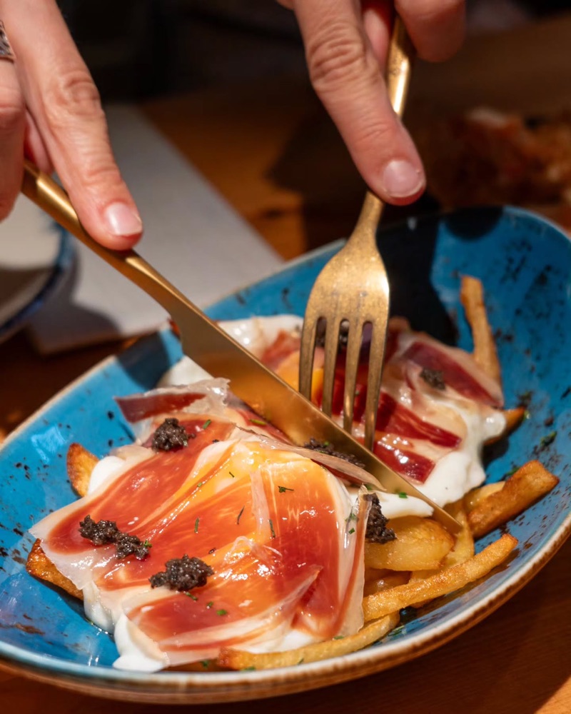 Algú talla uns ous trencats amb pernil i tòfona, en un bol blau